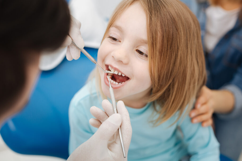 A little girl is getting a tooth cleaning from a dentist.