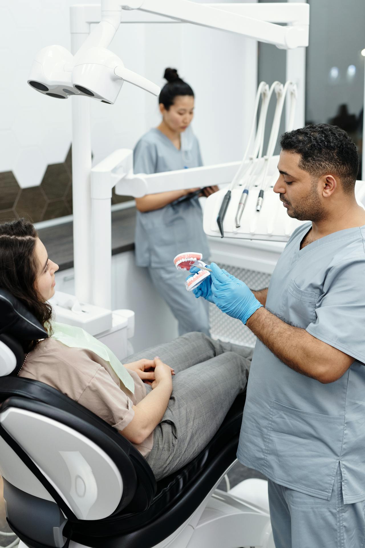 Dentist explaining treatment using a plastic teeth model during a patient consultation